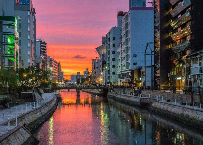 Fukuoka at sunset. The pinks and oranges of the sky are reflected on the river's surface.